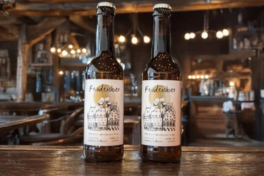 Beschwipster Nachtwächter (Hauptbild).jpg Zwei Flaschen Friedelnsbier stehen in einem rustikalen Wirtshaus mit stimmungsvoller Beleuchtung.