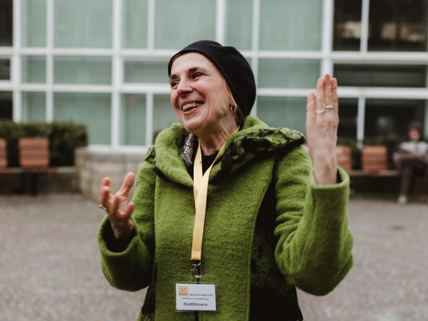 Altstadt-Highlights (2).jpg Ældre kvinde i grøn frakke og sort kasket griner hjerteligt på et torv i byen.