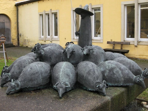 Gertrudenberg (3).jpg Bronze sculpture of twelve sheep and a shepherd with a hat in front of a yellow building in Osnabrück.