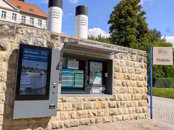 The photo shows ticket sales at the steamboat landing stage in Bad Schandau in front of a stone wall.