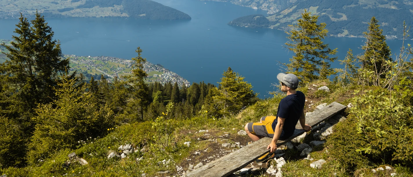 Ein Wanderer geniesst die Aussicht auf einer Bank auf dem Stollen auf der Klewenalp.