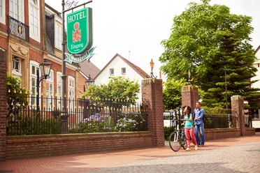 Radler vor Haus Russell vom Burghotel in Haselünne - Radfahren im Emsland ©Emsland Tourismus GmbH (2).jpg Zwei Radfahrer gehen vor dem historischen Burghotel Haselünne entlang einer Baumallee im Emsland.