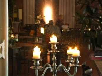 IMG_2946.JPG Kerzenständer mit brennenden Kerzen steht in einem dimm beleuchteten Raum mit verschwommenen Personen.Candlestick with burning candles stands in a dimly lit room with blurred people.