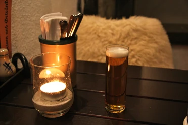 IMG_3073.JPG Candle and beer glass on wooden table next to cutlery holder, warm and cozy ambience.