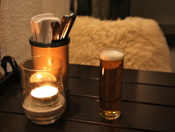 IMG_3073.JPG Kerze und Bierglas auf Holztisch neben Besteckhalter, warmes und gemütliches Ambiente.Candle and beer glass on wooden table next to cutlery holder, warm and cozy ambience.