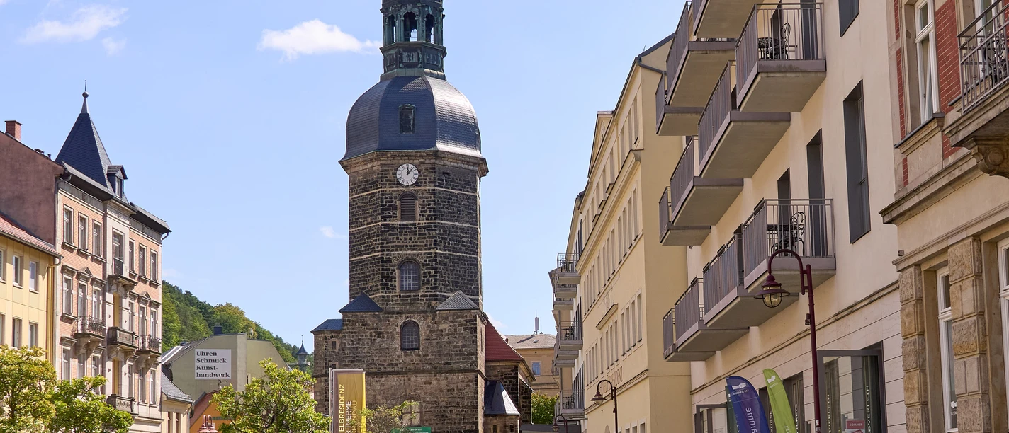 Street scene with people, church tower and historic buildings in the sunshine on the market square in Bad Schandau.