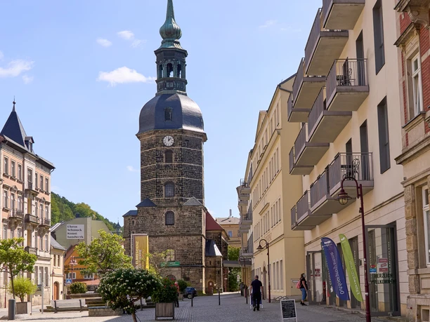 Street scene with people, church tower and historic buildings in the sunshine on the market square in Bad Schandau.