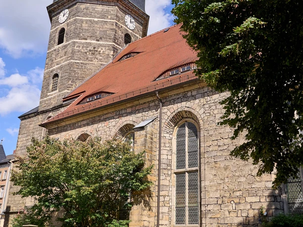 Kirche Bad Schandau Seiteneingang Bad Schandau church with stone façade and tower, surrounded by trees and blue sky.