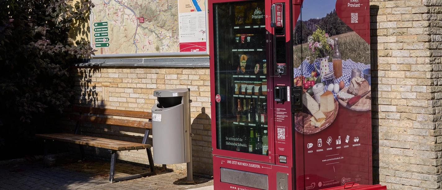 Vending machine with regional products in front of a map and a bench.