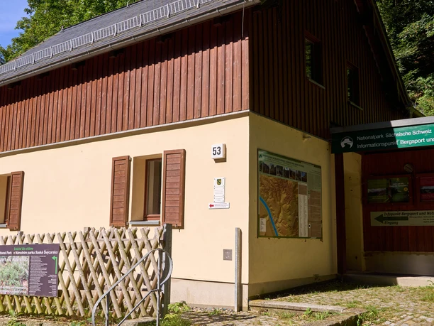 House with red roof and yellow walls, number 53, next to information stand.