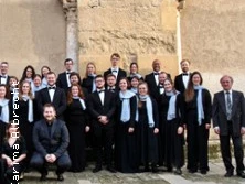 Eine Gruppe von Menschen in formeller Kleidung posiert vor einer alten steinernen Gebäudewand.