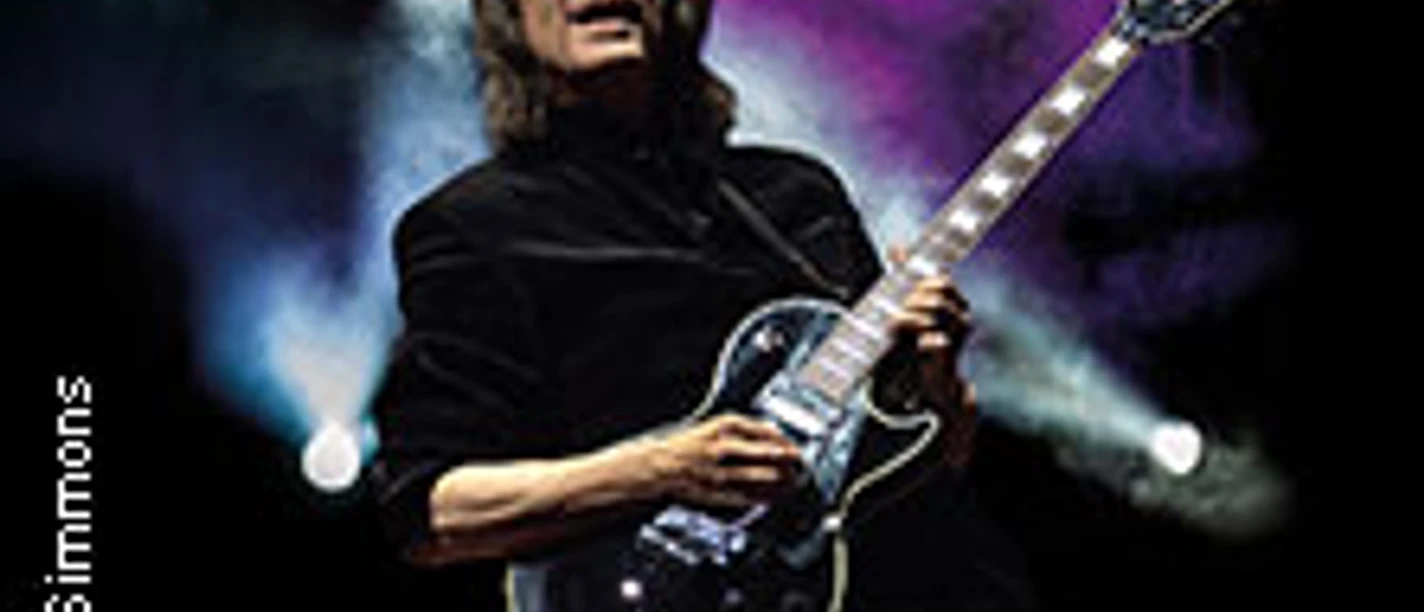 Steve Hackett spielt Gitarre auf einer dunklen Bühne, umgeben von bunten Lichteffekten.