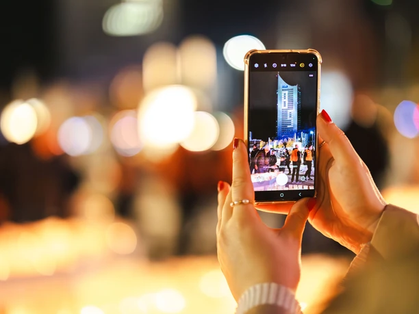 Person hält ein Smartphone, das eine nächtliche Stadtlandschaft mit einem beleuchteten Gebäude zeigt.