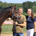 Live Training 1 (c) CHIO Aachen CAMPUS.jpg Zwei Menschen stehen lächelnd neben einem Pferd auf einem Rasenplatz an einem sonnigen Tag.