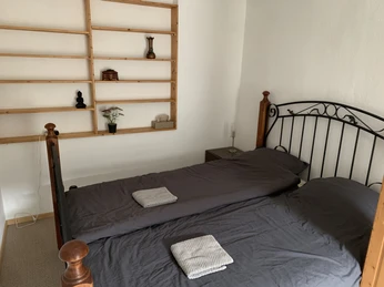 Schlafzimmer der Ferienwohnung Rad und Ruhe Zwei Einzelbetten mit grauer Bettwäsche, rustikales Kopfteil. Schlichter Holzboden und Regal.