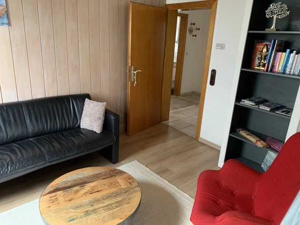 Wohnzimmer der Ferienwohnung Rad und Ruhe Wohnzimmer mit schwarzem Sofa, rotem Sessel, Couchtisch und Bücherregal an der Wand.