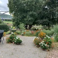 Garten und Weserblick der Ferienwohnung Rad und Ruhe Idyllischer Garten mit Blumen und Baumbestand, Gartenmöbeln, im Hintergrund Blick auf die Weser und Weserbrücke