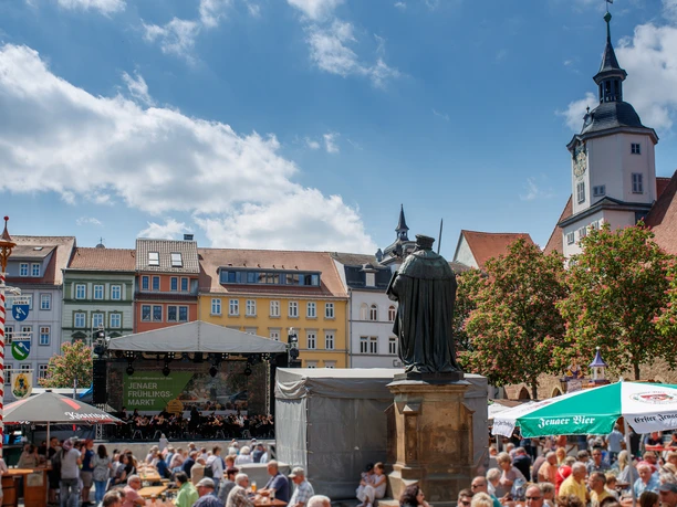 JenaerFrühlingsmarkt©JenaKultur_Moebius20249643c.jpg Szenerie des Jenaer Frühlingsmarktes mit Bühne, vielen Menschen, die sich um die Statue des Hanfriedes versammeln.