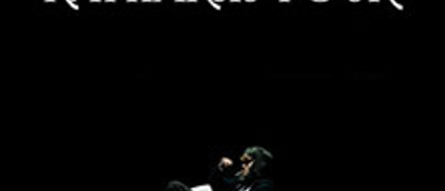 Zwei Personen sitzen auf einer Bühne in einem dunklen Raum, beleuchtet von einem einzelnen Scheinwerfer.