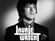 Schwarz-weiß Porträt von Laurie Wright mit Hut und gemusterter Krawatte, ernst blickend.