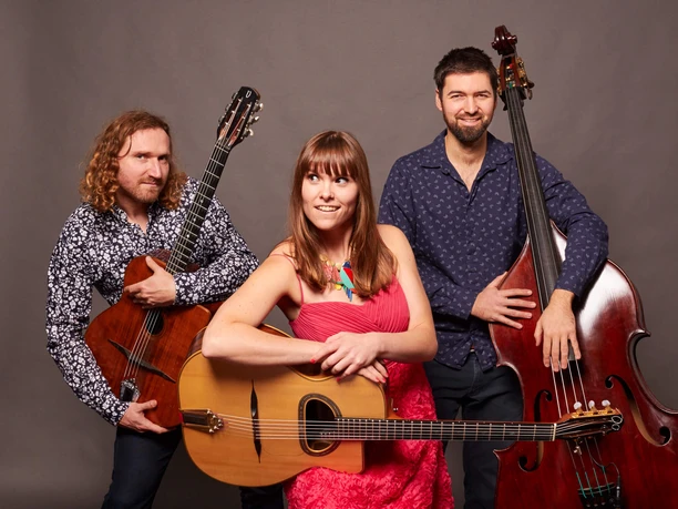 Marion und Sabo Band Drei Musikerinnen und Musiker mit Akkustikgitarre, Kontrabass und Gesang stehen lächelnd zusammen.