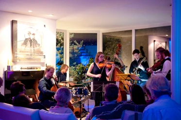 Musik in den Häusern der Stadt 2017 A group of musicians plays in a modern, well-lit room in front of a seated audience.