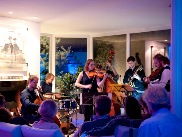 Musik in den Häusern der Stadt 2017 A group of musicians plays in a modern, well-lit room in front of a seated audience.