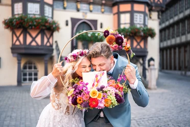 Hochzeitmesse Brautpaar mit Blumenkranz und Hochzeitstorte vor Fachwerkhäusern in Wernigerode.