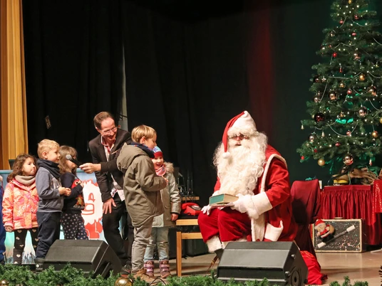 Schkeuditzer Weihnachtsmarkt - Weihnachten in der Region Leipzig Der Weihnachtsmann sitzt neben einem geschmückten Baum und übergibt den Kindern Geschenke.