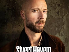 Sivert Høyem posiert vor einem dezenten Hintergrund. Der Künstler steht frontal und blickt ernst.