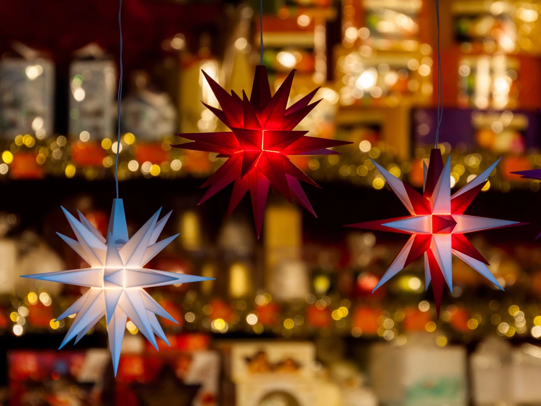 AdobeStock_99289018.jpeg Leuchtende Weihnachtssterne in Rot und Weiß vor warm beleuchtetem Marktstand im Hintergrund