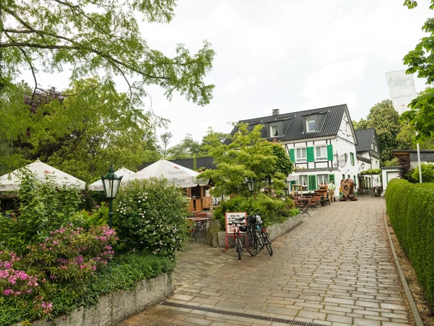 Restaurant "Kleine Schweiz" in Velbert Ein rustikales Fachwerkgebäude umgeben von blühenden Gärten und schattigen Bäumen.