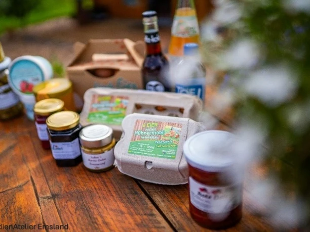 Bild Produkte mit ©n.JPG Regionale Produkte wie Eier, Marmelade und Getränke auf Holztisch im Grünen arrangiert.