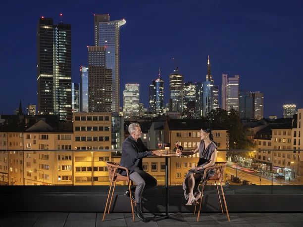 Oaks Bar NH Collection Frankfurt Spin Tower Paar mit Drinks auf Dachterrasse, Skyline Frankfurt bei Nacht