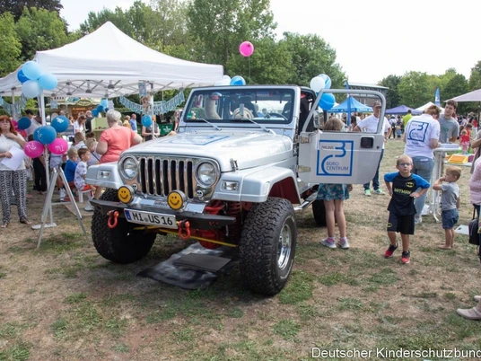 Eine Stadt für alle.jpg Auf dem Bild ist ein Auto mit vielen Kinder drumherum abgebildet