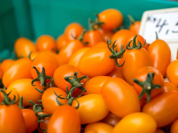 Auf dem Bild sind viele kleine orangene Tomaten zu sehen. Im Hintergrund befindet sich ein Preisschild.