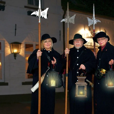 Nachtwächter-Rundgang in Meppen ©Tourist Information Meppen.jpg Drei Nachtwächter in historischen Gewändern mit Hellebarden und Laternen vor Meppener Hausfassade