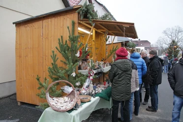 Festlich geschmückter Weihnachtsmarktstand mit handgefertigten Waren, vor dem sich Besucher umschauen und stöbern