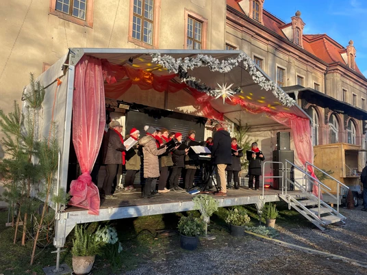 Brandiser Schlossweihnacht - Weihnachten in der Region Leipzig Im Schlosspark Brandis singt ein Chor auf einer festlich dekorierten Bühne während des Weihnachtskonzerts.