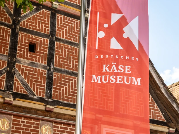 Nieheim-Deutsches-Kaesemuseum-Teutoburger-Wald-Stadt-Nieheim-D-Ketz-226.jpg Rotes Banner des Deutschen Käsemuseums vor historischem Fachwerkhaus in Nieheim.