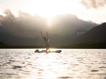 Sunset yoga on the lake Frau macht SUP Yoga Bettmersee im Sommer bei Sonnenuntergang mit goldener Spiegelung auf der Wasseroberfläche und Bergen im HintergrundWoman doing SUP Yoga Bettmersee in summer at sunset with golden reflection on the water surface and mountains in the backgroundFemme faisant du SUP Yoga Bettmersee en été au coucher du soleil avec un reflet doré à la surface de l'eau et des montagnes en arrière-plan