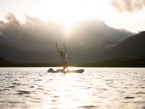 Sunset yoga on the lake Woman doing SUP Yoga Bettmersee in summer at sunset with golden reflection on the water surface and mountains in the background