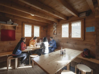Cozy break in the mountain hut Teilnehmer der 2-Tage-Gletschertour Aletschgletscher sitzen in rustikaler Hütte beisammen und genießen eine Rast im WallisParticipants on the 2-day Aletsch Glacier tour sit together in a rustic hut and enjoy a break in ValaisLes participants à la randonnée de 2 jours sur le glacier d'Aletsch sont assis ensemble dans une cabane rustique et profitent d'une pause en Valais.
