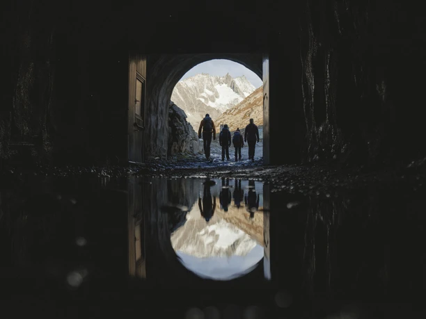 Exit through the Tälligrat Tunnel Participants on the Aletsch Glacier round tour leave the Tälligrat Tunnel with a view of snow-covered mountains and rocks