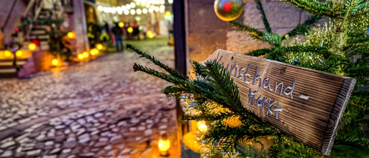 Adventsmarkt_Packhof_2024-1(1).jpg Uniek verlichte adventsmarkt met geplaveid pad, feestelijke versieringen met sparrentakken en feeërieke lichtjes.