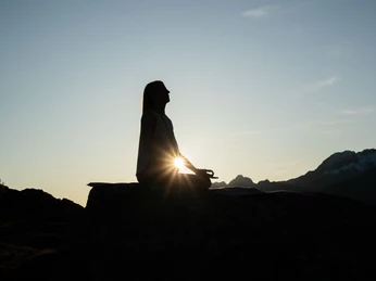 Yoga silhouette in the evening light Frau meditiert im Lotussitz auf einem Felsen beim Sonnenuntergang Yoga Aletsch Arena mit Blick auf die BergeWoman meditating in the lotus position on a rock at sunset Yoga Aletsch Arena with a view of the mountainsFemme méditant en position du lotus sur un rocher au coucher du soleil Yoga Aletsch Arena avec vue sur les montagnes