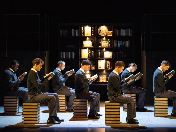 Der Club der toten Dichter.jpg Das Bild zeigt sieben Schüler, die jeweils akkurat auf einem Holzhocker in einer Bibliothek sitzen und Bücher lesen.