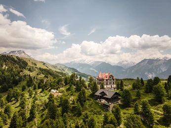 Luftaufnahme Villa Cassel inmitten der Berge Kräuterwanderung Aletsch Arena mit Panorama auf die Villa Cassel, eingebettet in die Bergwelt und den AletschwaldAletsch Arena herb hike with panoramic views of Villa Cassel, nestled in the mountains and the Aletsch ForestRandonnée sur le thème des herbes aromatiques dans l'Aletsch Arena avec panorama sur la Villa Cassel, nichée dans le paysage montagneux et la forêt d'Aletsch