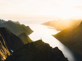 Norwegen Felsige Berglandschaft im Vordergrund, dahinter ein einsamer Wanderer, mit Blick auf das sonnenbeschienene Fjord.Rocky mountain landscape in the foreground, behind it a lone hiker, with a view of the sunlit fjord.