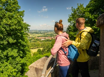 Teutoburger-Wald-Stadt-Nieheim-D-Ketz-127.jpg Zwei Menschen mit Rucksäcken blicken von einer Aussichtsplattform auf Nieheim und die Landschaft.